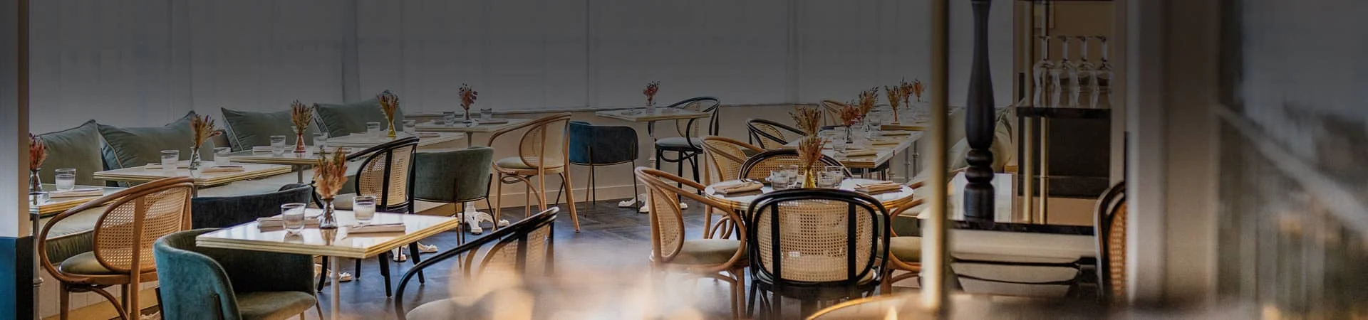 Salle du restaurant Bistrot Yonnais à La Roche-sur-Yon dressée pour le menu de la Saint-Sylvestre, avec chaises cannées, banquettes en velours vert et bouquets de fleurs séchées