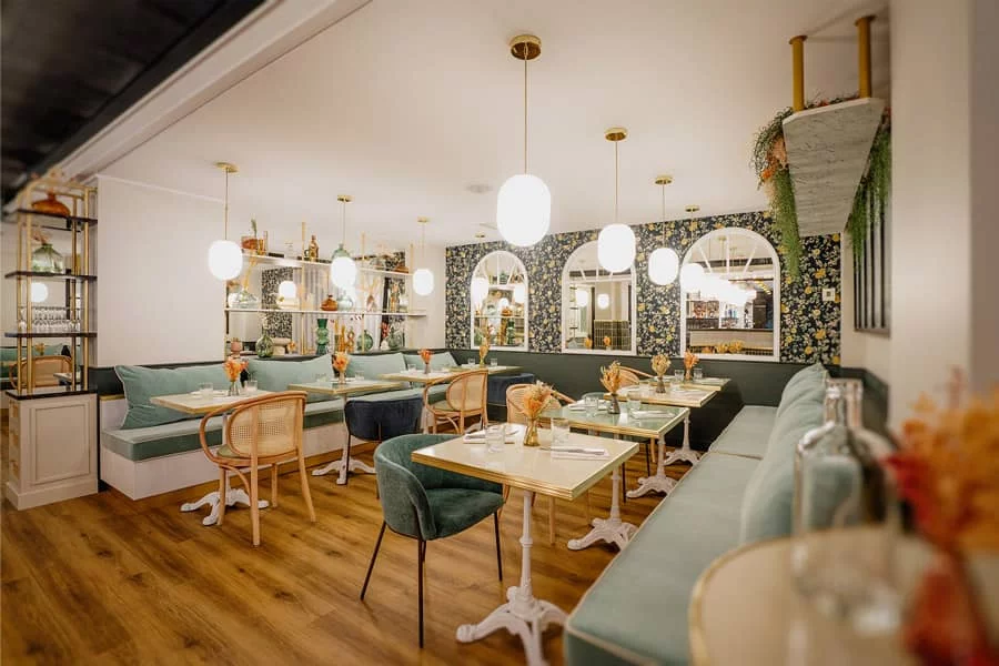 Salle intérieure du Bistro Yonnais avec banquettes vertes, tables en bois clair, chaises en rotin et luminaires suspendus, dans une ambiance chaleureuse et élégante.