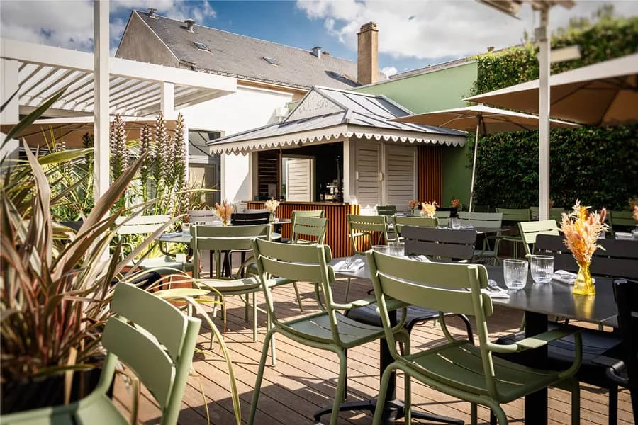 Terrasse extérieure du Bistro Yonnais avec tables et chaises vert olive, plantes décoratives et parasols, offrant un cadre calme et verdoyant en plein air.